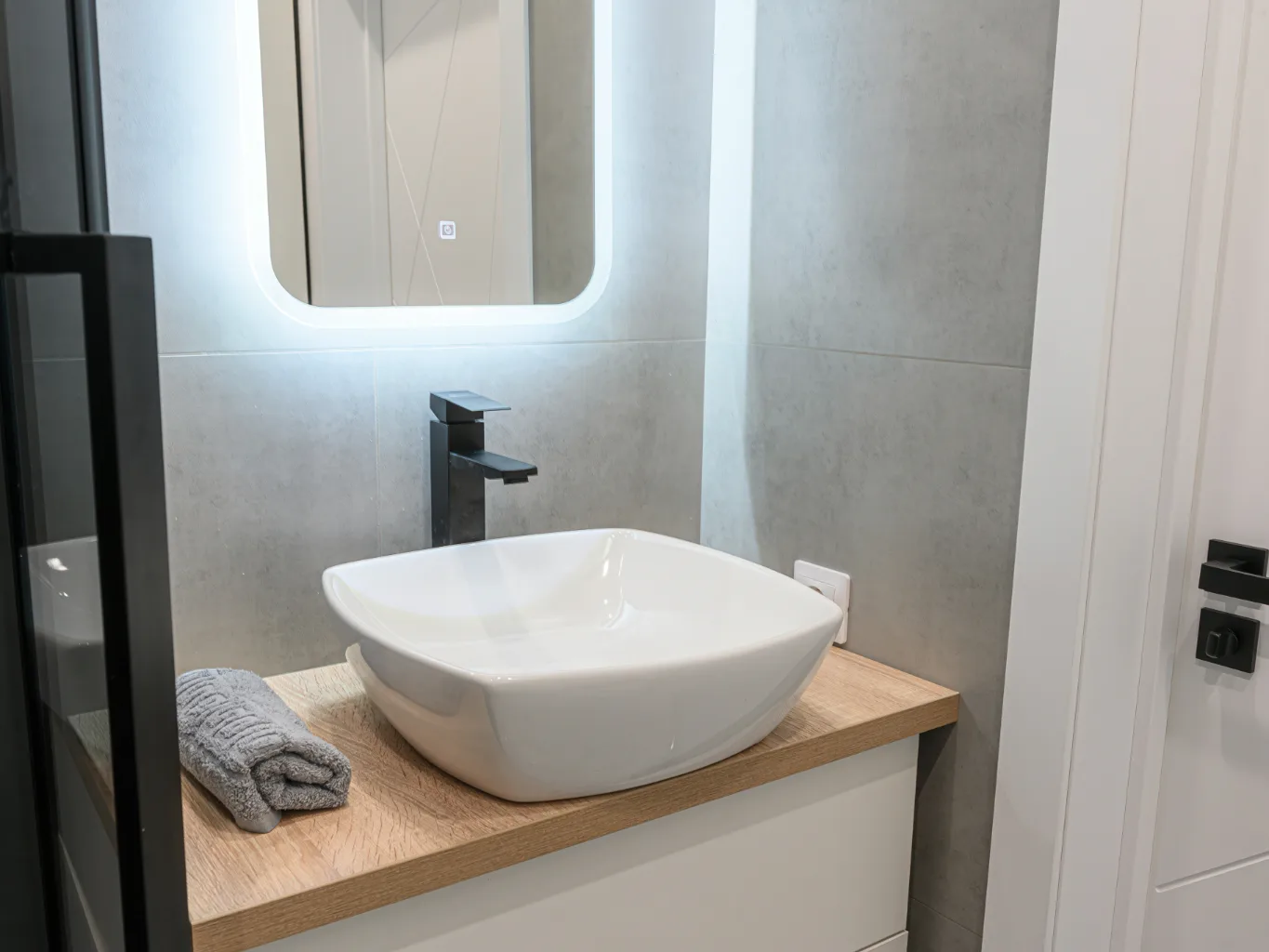 A plumber working on a residential fixture & vanity installation job — mid-task, hands, tools and the work itself in sharp focus, the rest of the space softly out of focus