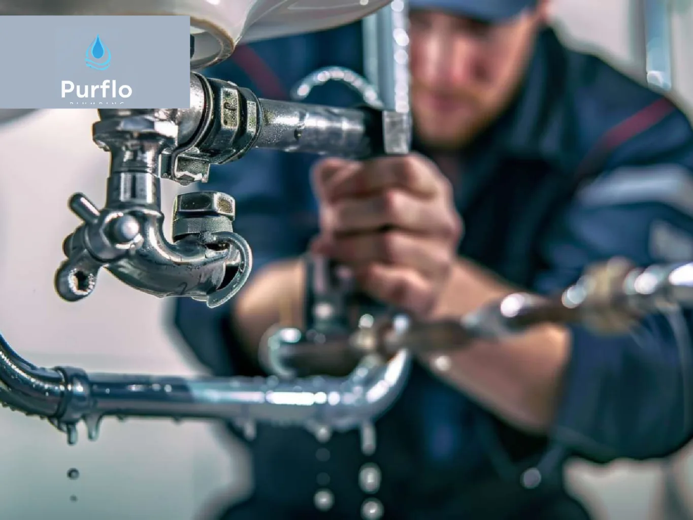 A plumber working on a residential commercial plumbing job — mid-task, hands, tools and the work itself in sharp focus, the rest of the space softly out of focus