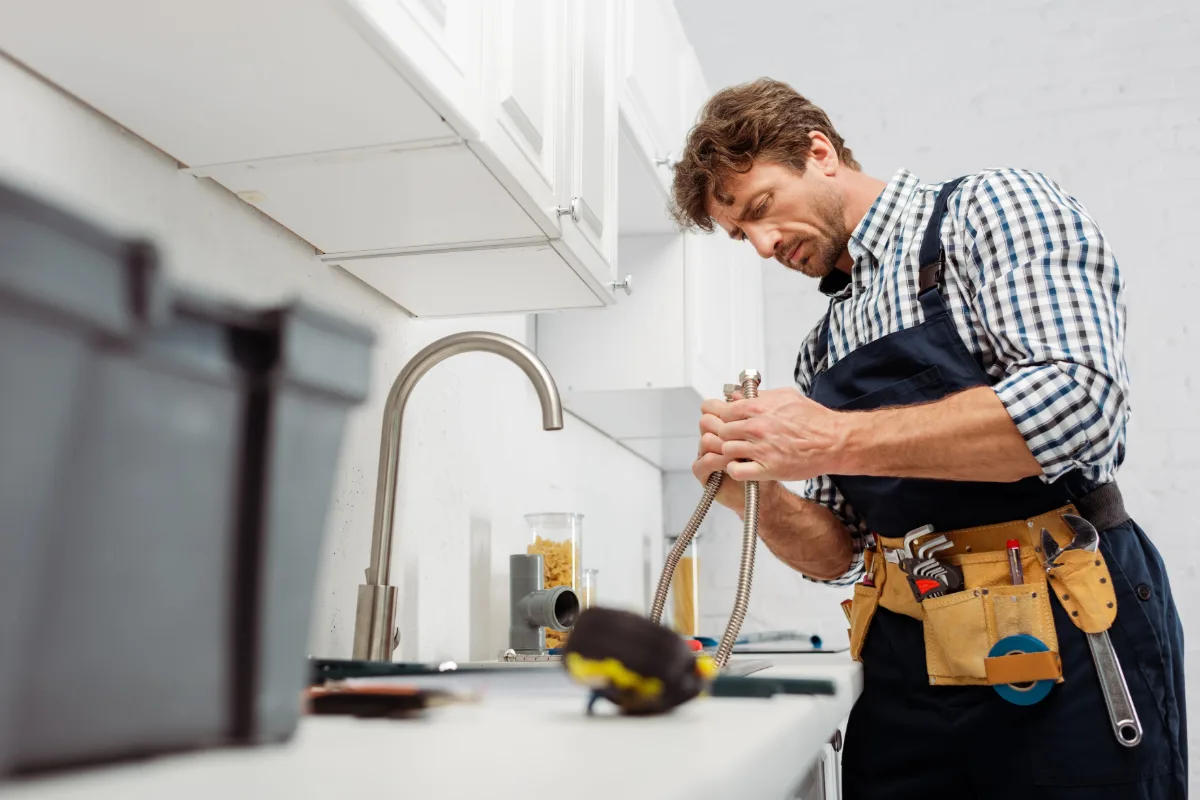A homeowner and a plumber reviewing plans together at a kitchen table, paperwork and a tape measure between them, both engaged in the conversation